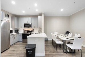 Uma cozinha moderna com armários brancos, eletrodomésticos de aço inoxidável e um espaço de refeições com cadeiras e mesa brancos.