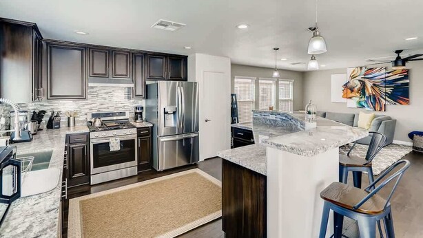 A modern kitchen with dark cabinets, stainless steel appliances, and a marble countertop. - Modern Pool House - 15min to the strip! (Las Vegas)