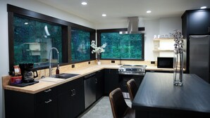 A modern kitchen with a large window, a built-in oven, and a dining area with a table and chairs. - NEW Build! Private cabin in the woods w/hot tub & convenient central location! (Whitefish)