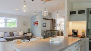 Cozinha moderna com ilha central, luminárias pendentes e área de refeições com sofá e mesa de centro.