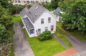A white two-story house with a sloped roof, a front porch, and an American flag. - Charming New Englander in the Heart of Ogunquit (Ogunquit)