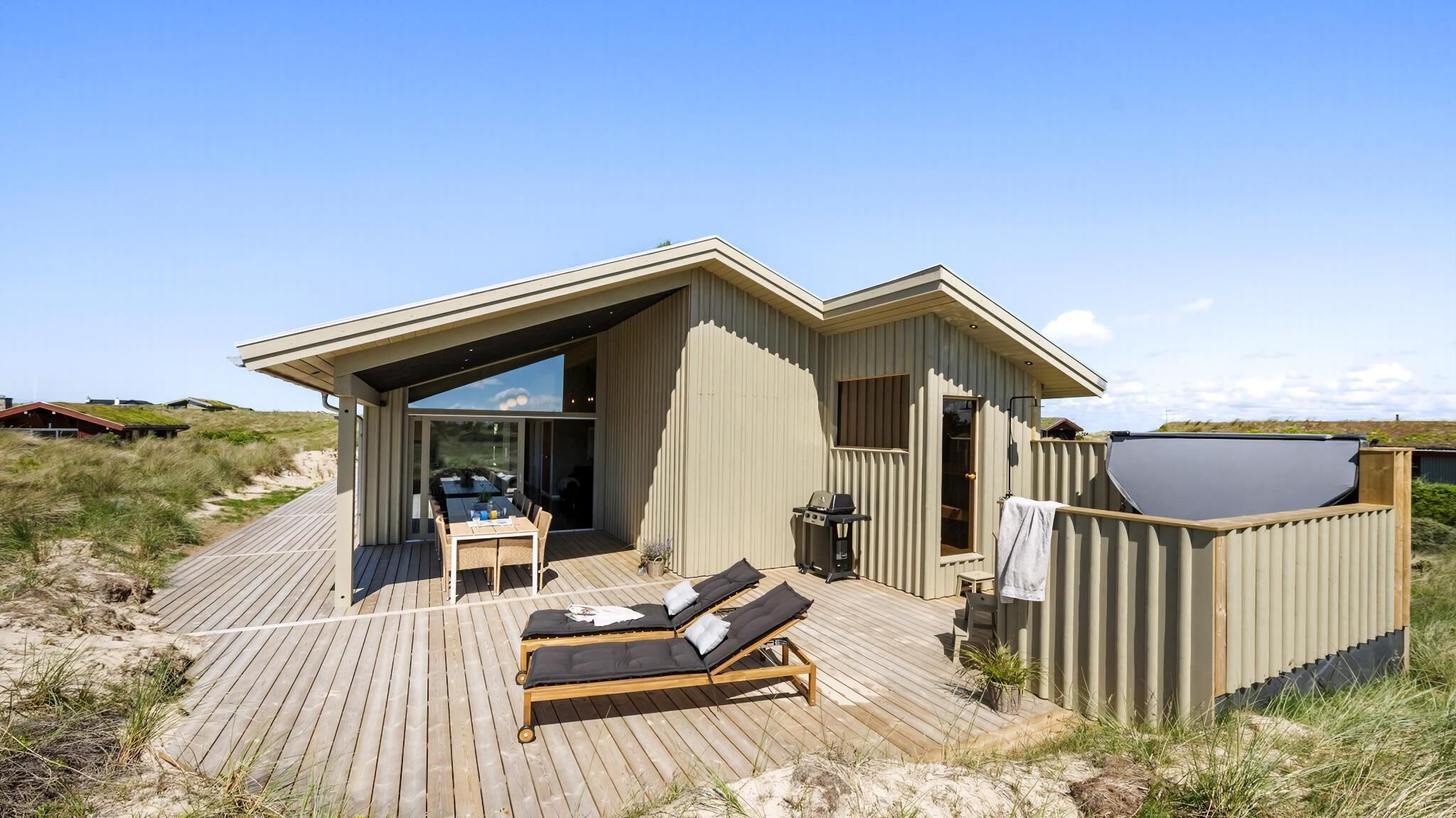 A modern beach house with a deck, outdoor seating, and a large window.