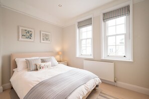 Ein Schlafzimmer mit einem Bett, zwei Nachttischen, einem Heizkörper und zwei mit Vorhängen versehenen Fenstern.