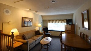 A room with a sofa, a small table, a dining table, a TV, and a window with a view. - Spend Your Vacation at Inns of Waterville Valley! (Waterville Valley)