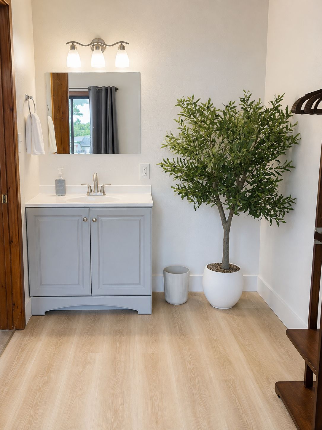 Een badkamer met een witte wastafel, een spiegel, een potplant en een prullenbak.