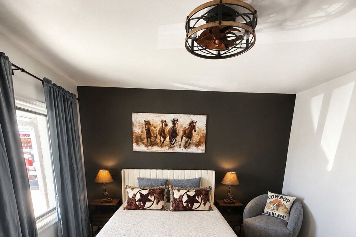 A bedroom with a bed, a chair, a lamp, a painting, and a ceiling light fixture.