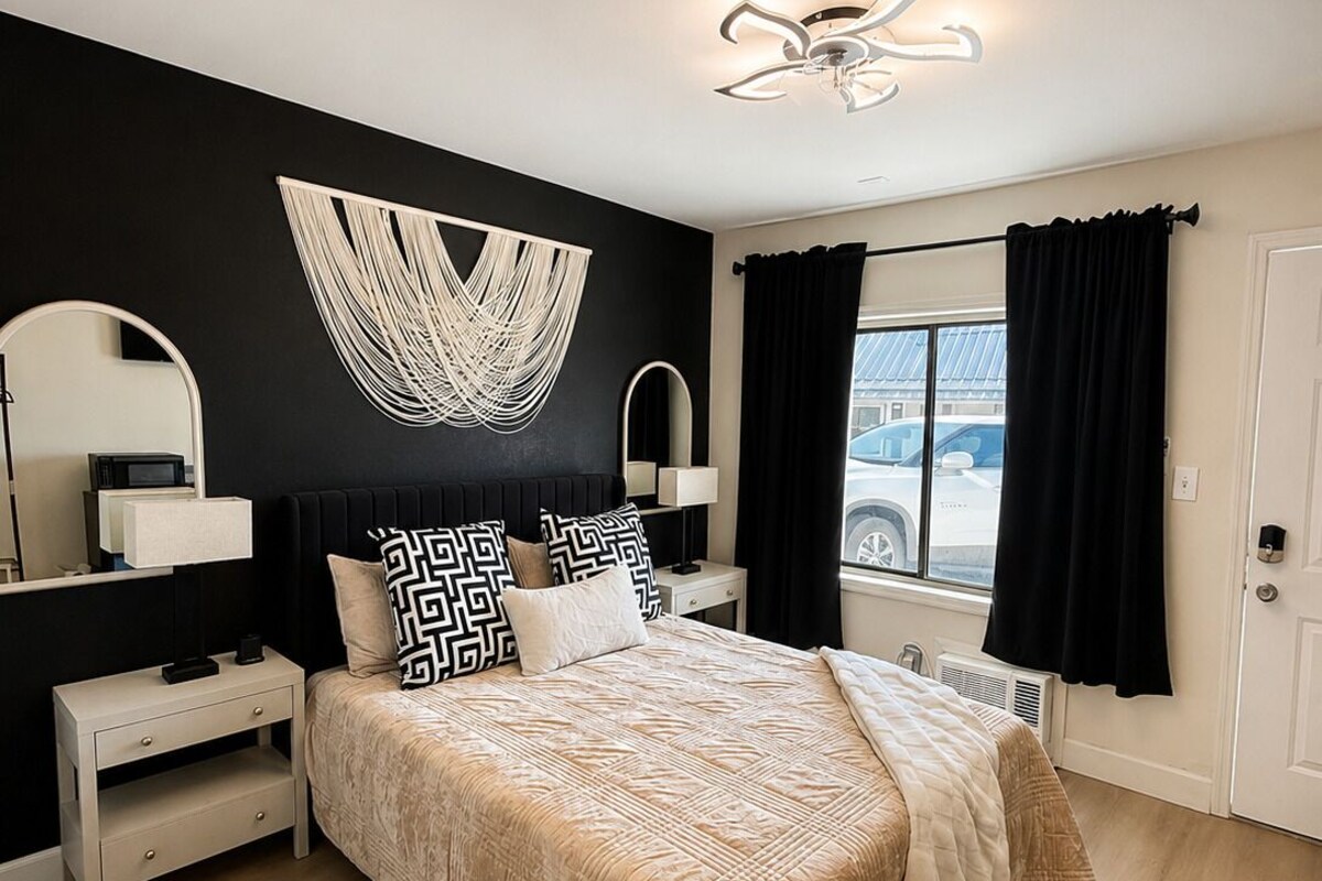 A bedroom with a bed, bedside tables, a chair, a large mirror, and a window with curtains.