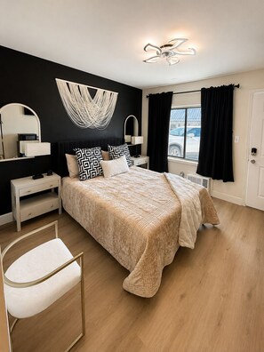 A bedroom with a bed, bedside tables, a chair, a large mirror, and a window with curtains.