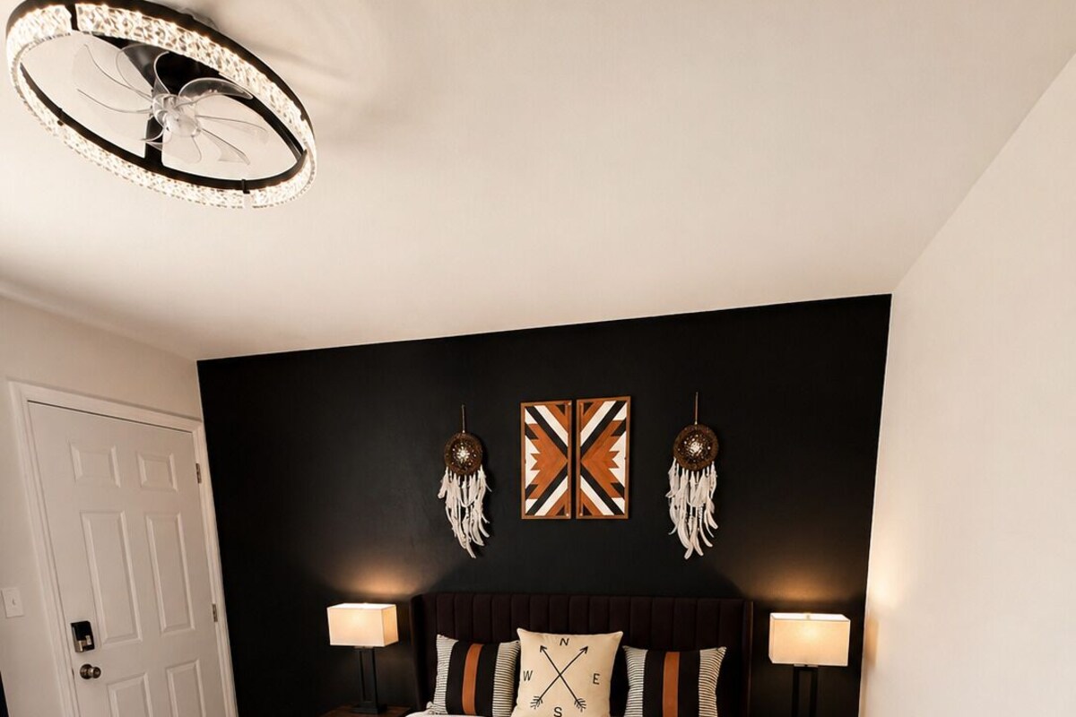 A bedroom with a bed, two bedside tables, a wall-mounted lamp, a ceiling light fixture, and a door.