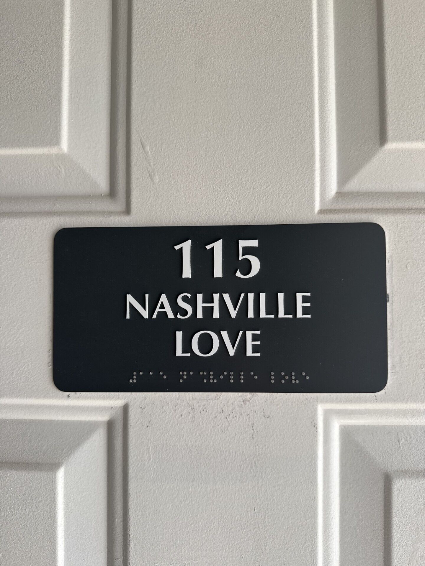 A black address plaque on a white door with the number 115 and the words 'Nashville Love' on it.