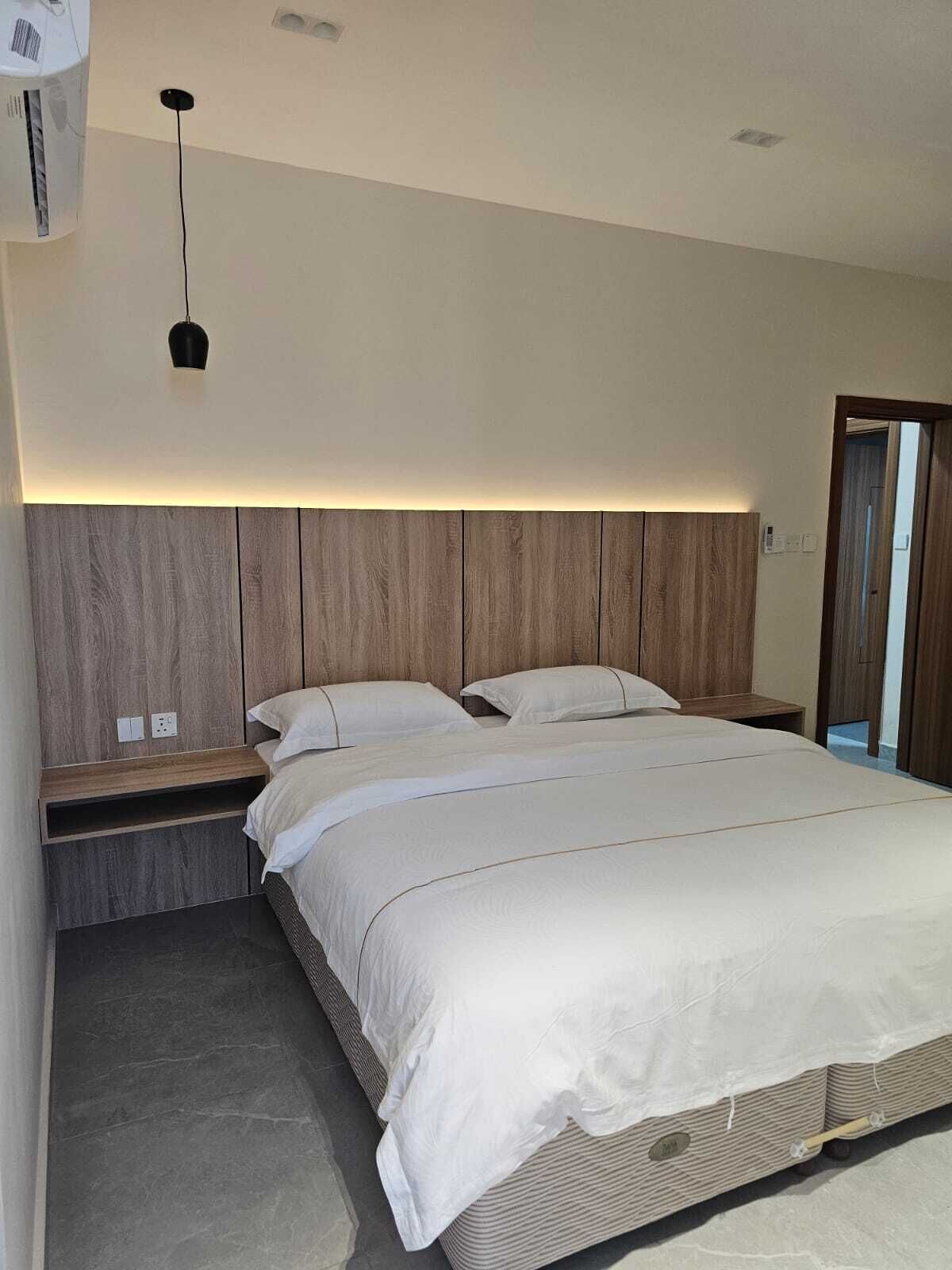 A modern bedroom with a wooden headboard, a bed with white bedding, a bedside table, and a wall-mounted air conditioning unit.