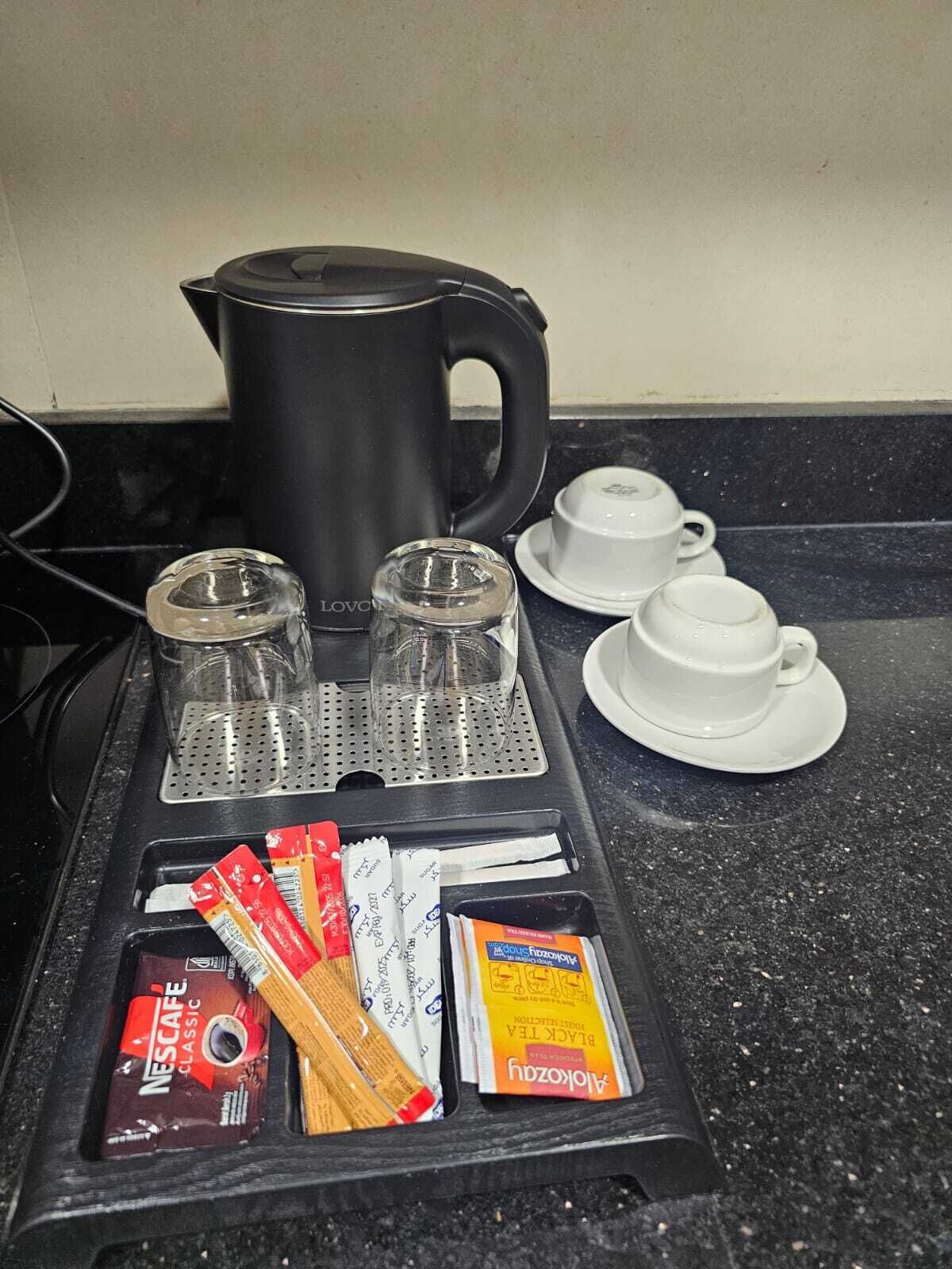 Una encimera de cocina con una cafetera, cuatro tazas y cápsulas de café.
