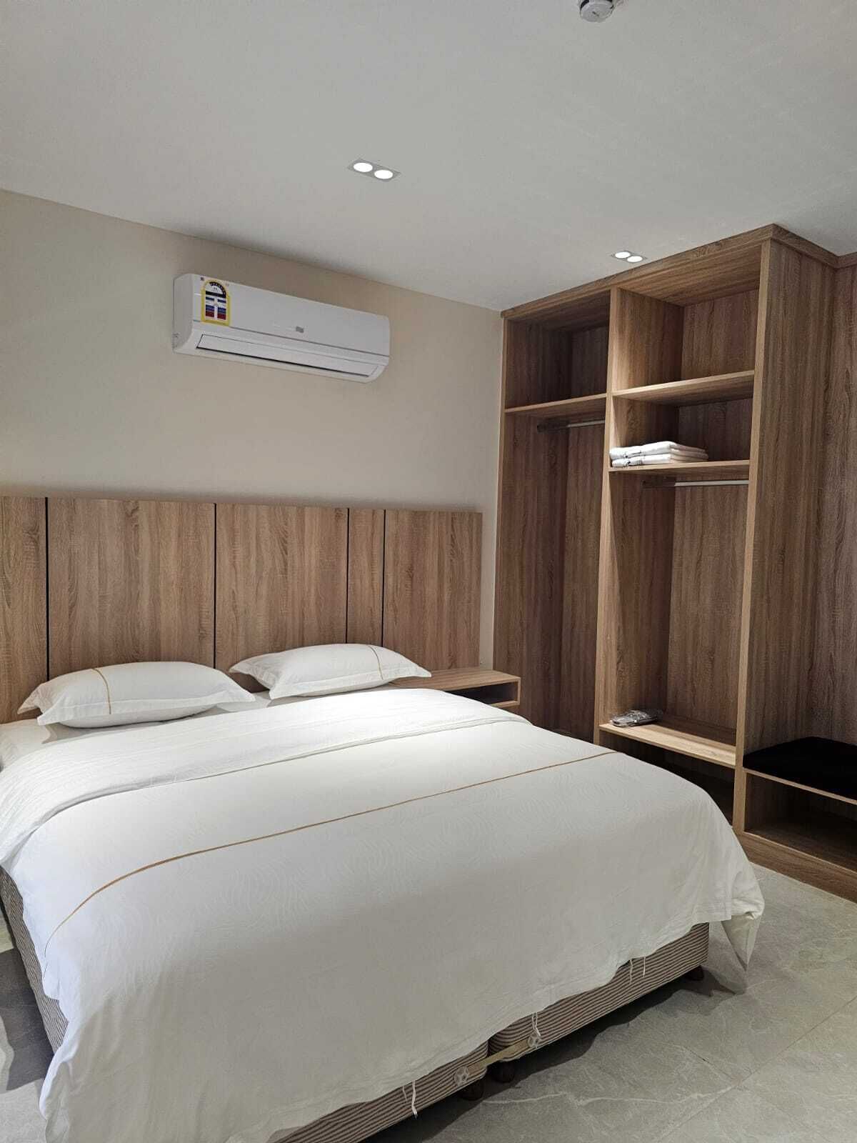 A bedroom with a bed, a wooden wardrobe, and an air conditioning unit.