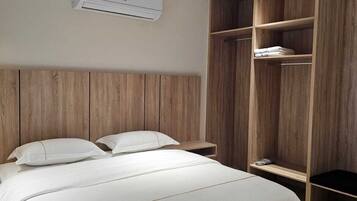 A bedroom with a bed, a wooden wardrobe, and an air conditioning unit.