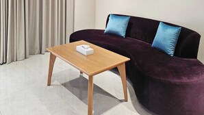 A modern living room with a dark purple sofa, a wooden coffee table, and a large window with beige curtains.