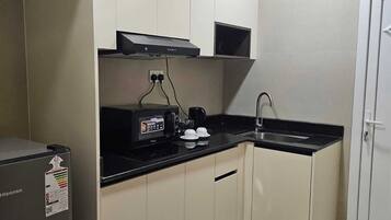 A compact kitchen with a refrigerator, a coffee maker, a microwave, and a sink.