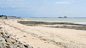 Ein sandiger Strand mit einem steinernen Wellenbrecher und ruhigem Meer.