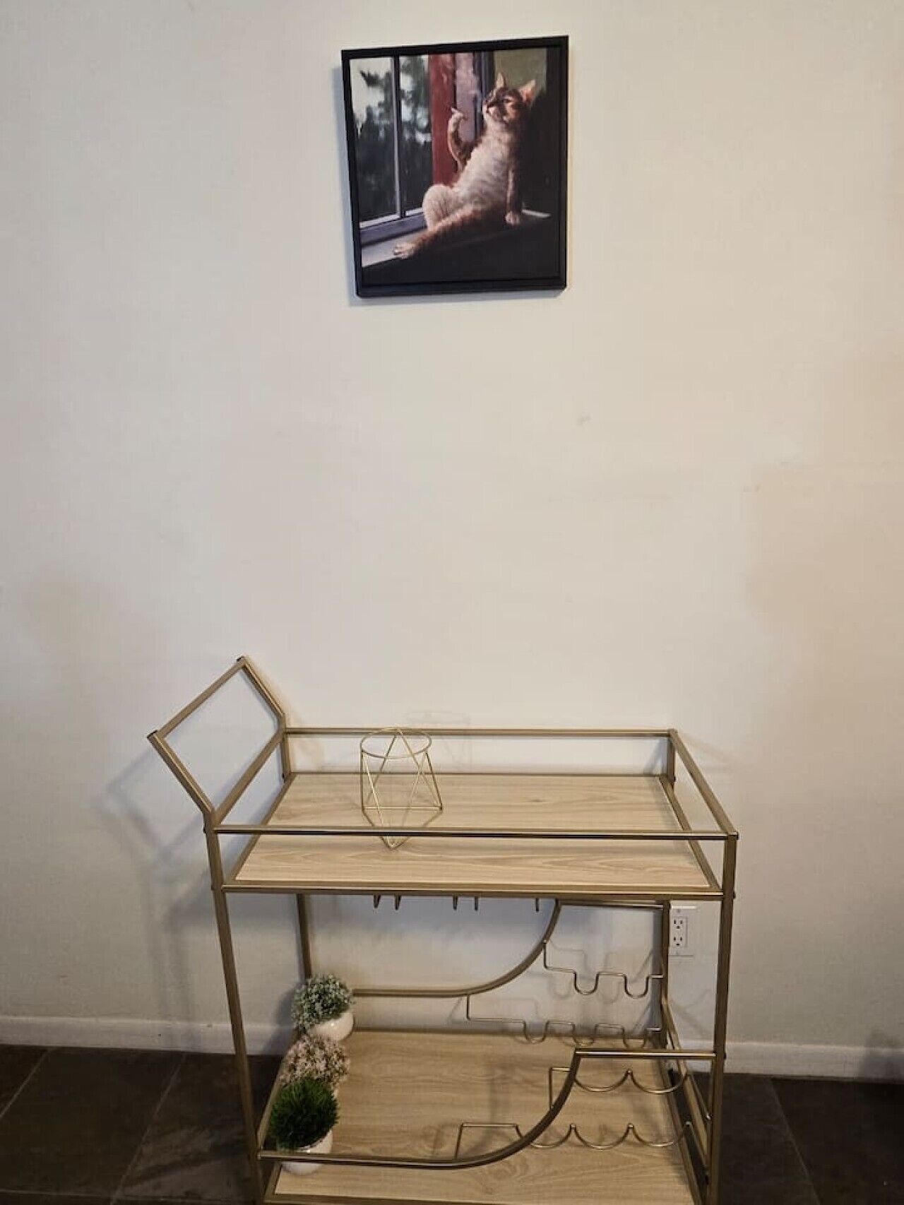Uma estante de metal com um vaso pequeno e um quadro na parede.