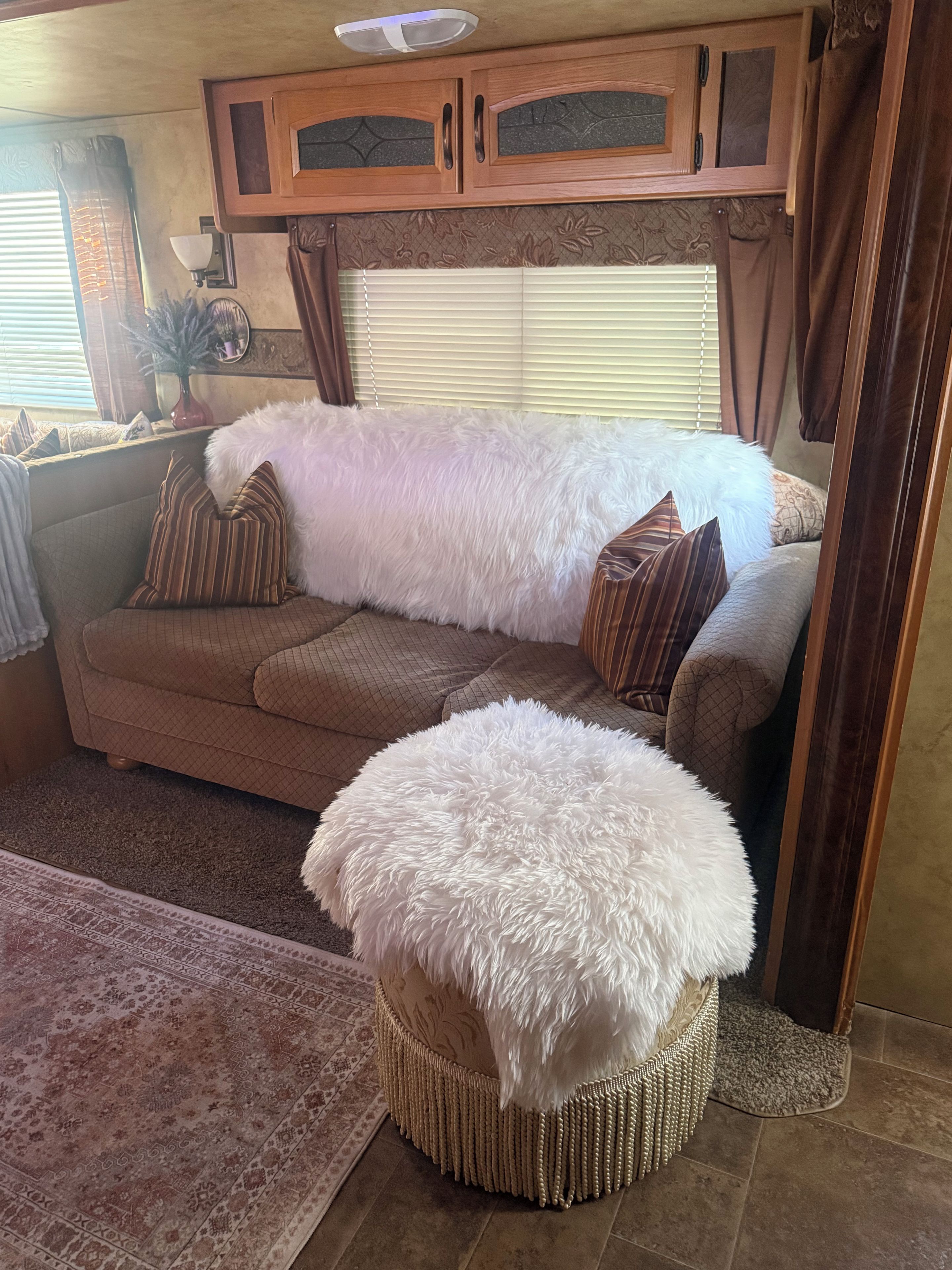 A cozy living area with a sofa, a large white fluffy ottoman, and a patterned rug.