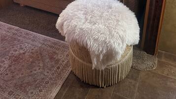 A cozy living area with a sofa, a large white fluffy ottoman, and a patterned rug.