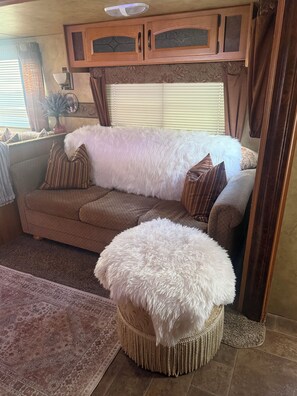 A cozy living area with a sofa, a large white fluffy ottoman, and a patterned rug.