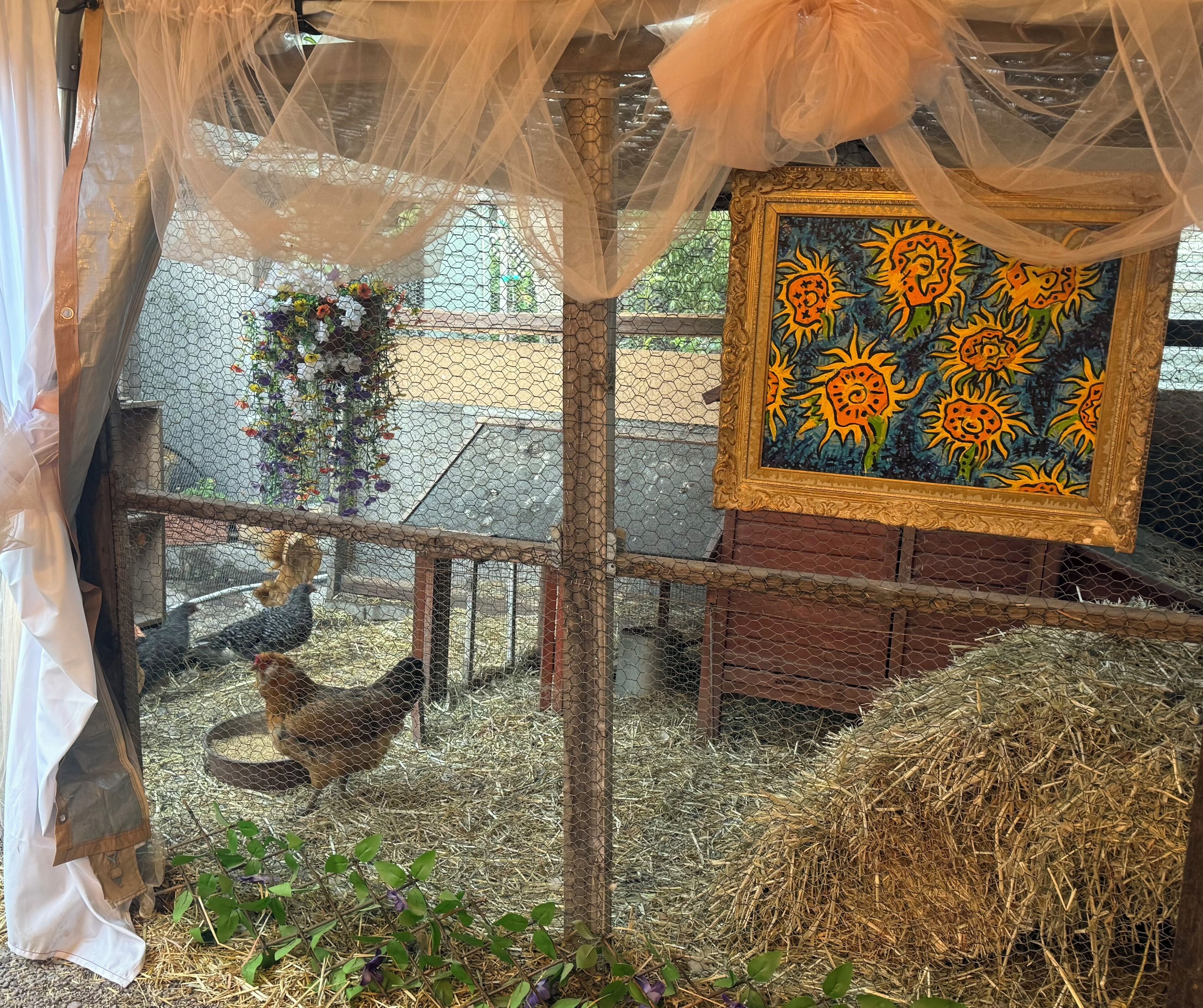 A rustic outdoor area with a chicken coop, hay bales, and a decorative painting.
