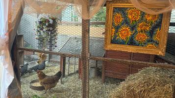 A rustic outdoor area with a chicken coop, hay bales, and a decorative painting.