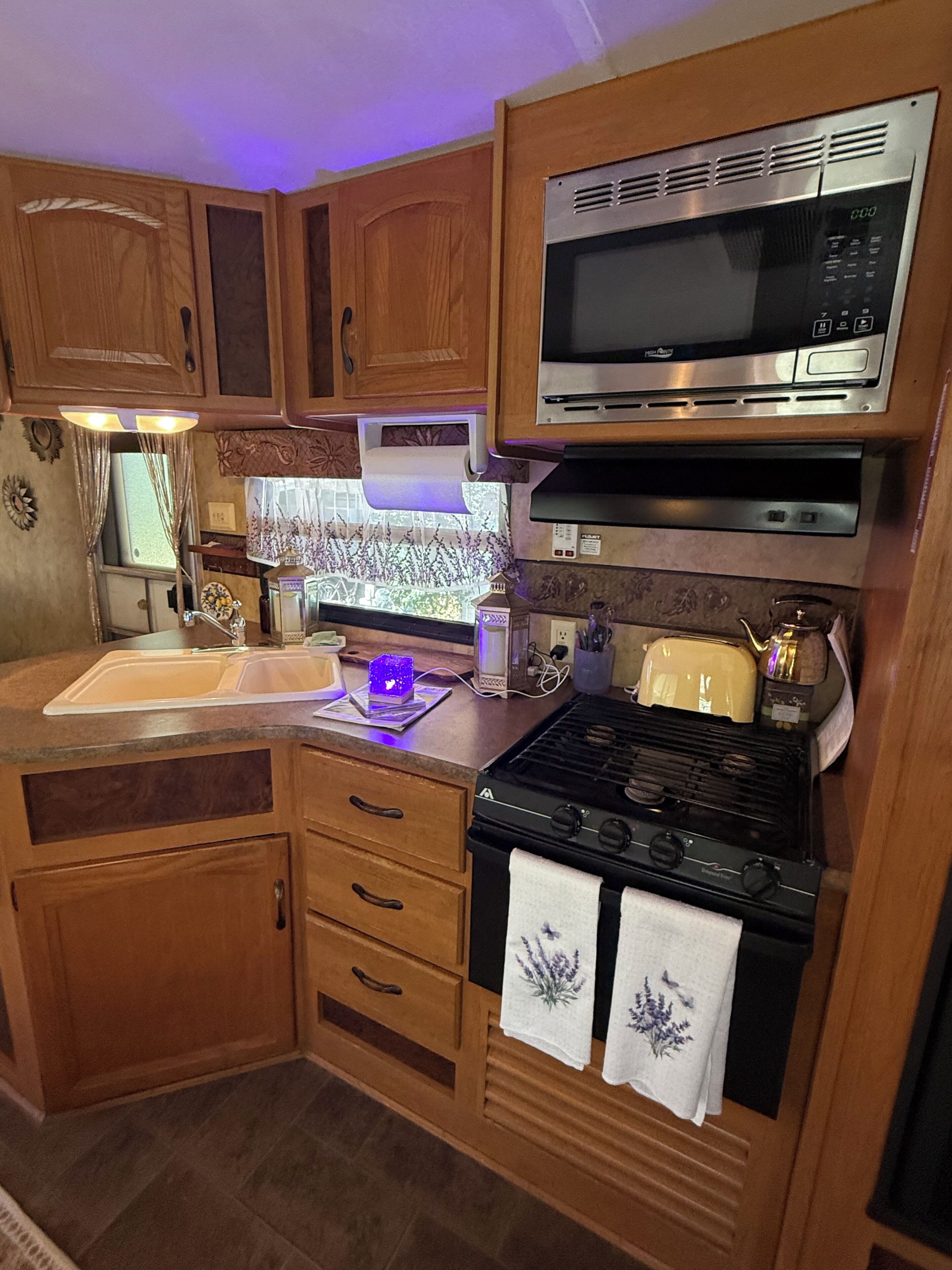 A compact kitchen with wooden cabinets, a microwave, a stove, and a sink.