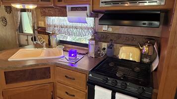 A compact kitchen with wooden cabinets, a microwave, a stove, and a sink.