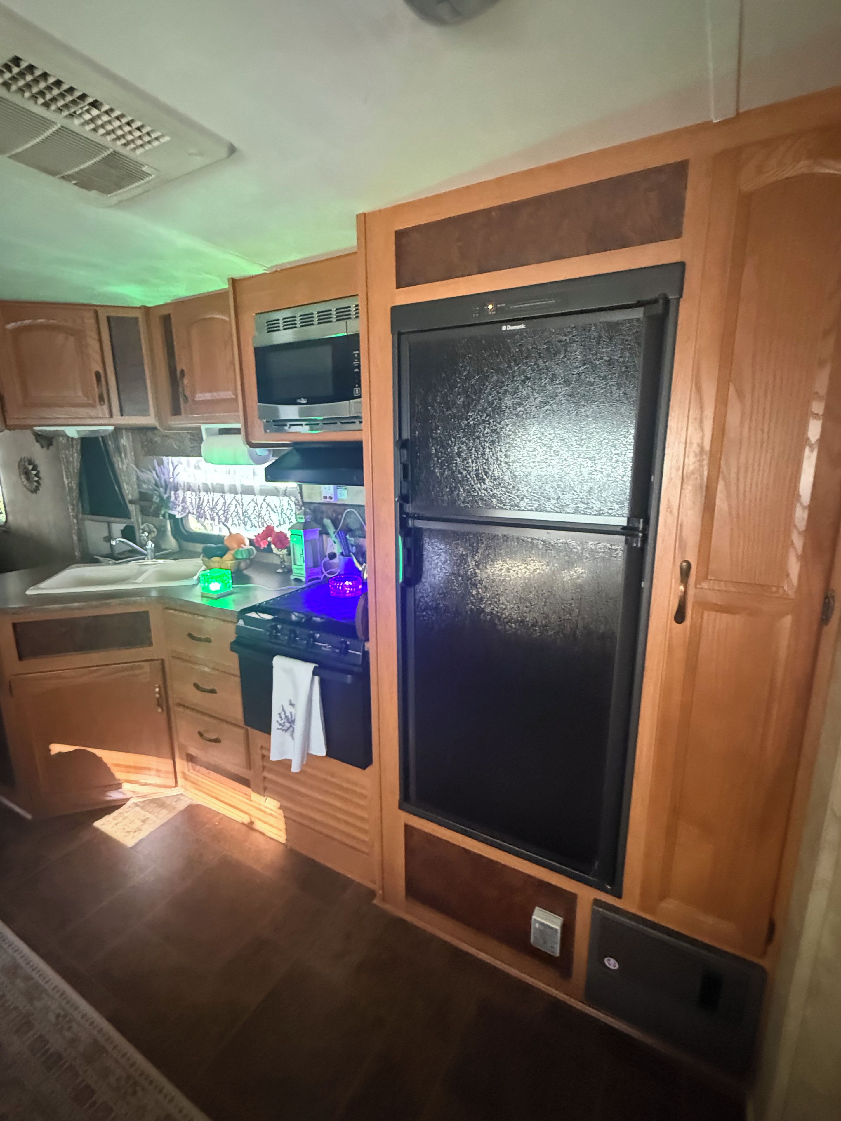 A compact kitchen with wooden cabinets, a black refrigerator, a microwave, and a gas stove.