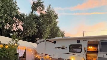 A recreational vehicle with 'HIDEOUT' branding, surrounded by artificial grass, outdoor furniture, and string lights.