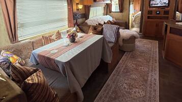 A cozy RV interior with a dining table, cushioned seating, a television, and a patterned rug.