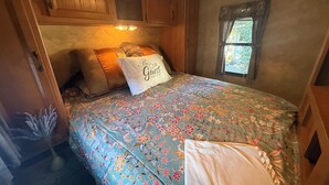 Quarto com colcha florida, travesseiro com a inscrição 'Be Our Guest', armários de madeira e janela com vista.