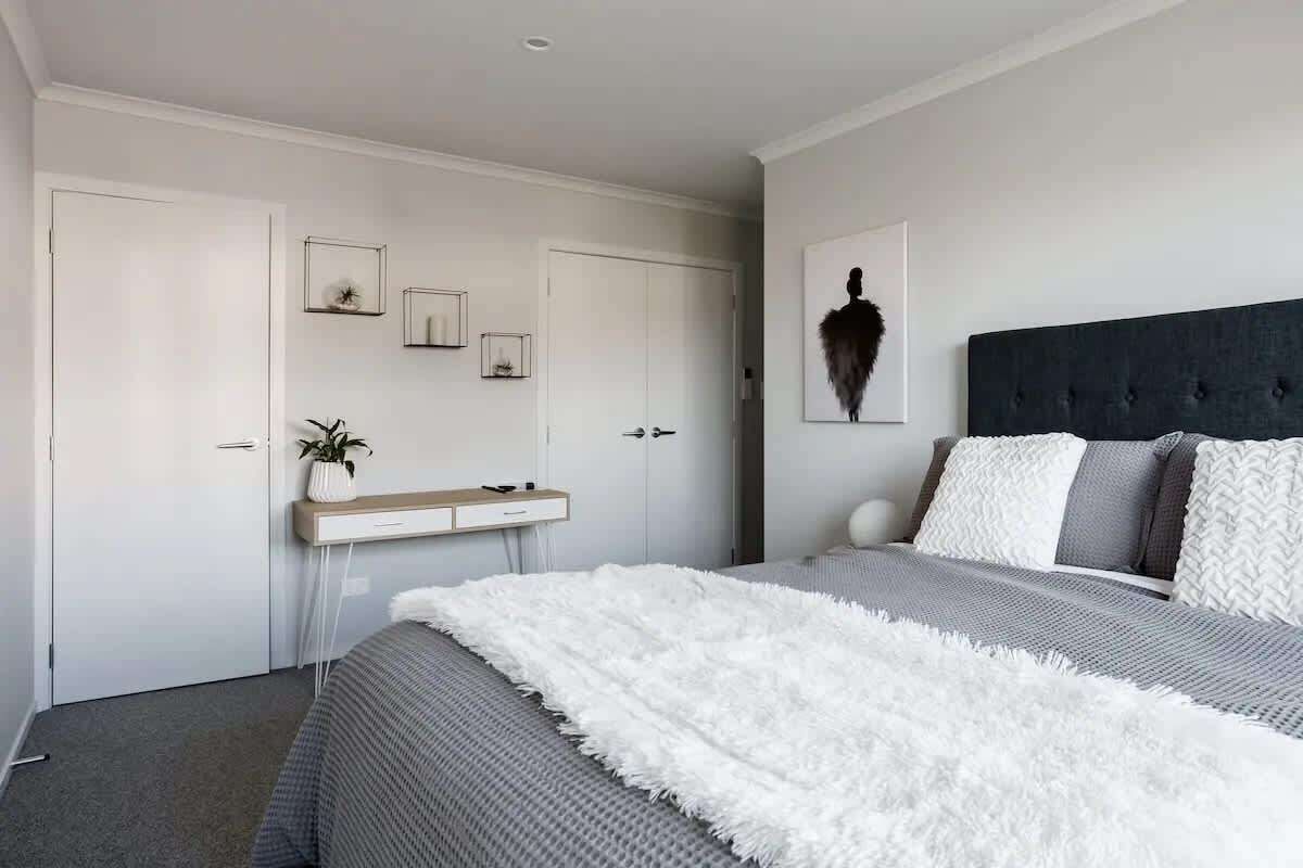 Ein Schlafzimmer mit einem Bett, einem Nachttisch, einem Spiegel und einem an der Wand hängenden Kunstwerk.