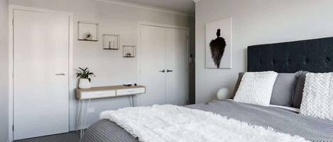 Ein Schlafzimmer mit einem Bett, einem Nachttisch, einem Spiegel und einem an der Wand hängenden Kunstwerk.