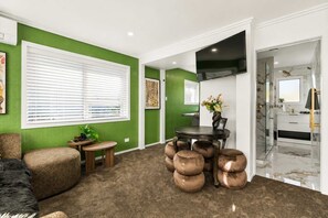 A room with a green accent wall, a round table with chairs, a sofa, and a mirror in the adjacent bathroom. - Winifreds Apartments - By Superior Stays (Hamilton)
