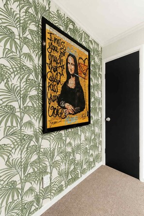 A framed artwork on a wall with a tropical leaf pattern wallpaper, a door, and a carpeted floor. - Winifreds Apartments - By Superior Stays (Hamilton)