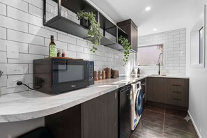 Une cuisine moderne équipée d’un four, d’un micro-ondes et d’un lave-vaisselle encastrés. On y trouve des placards, un plan de travail et une fenêtre.