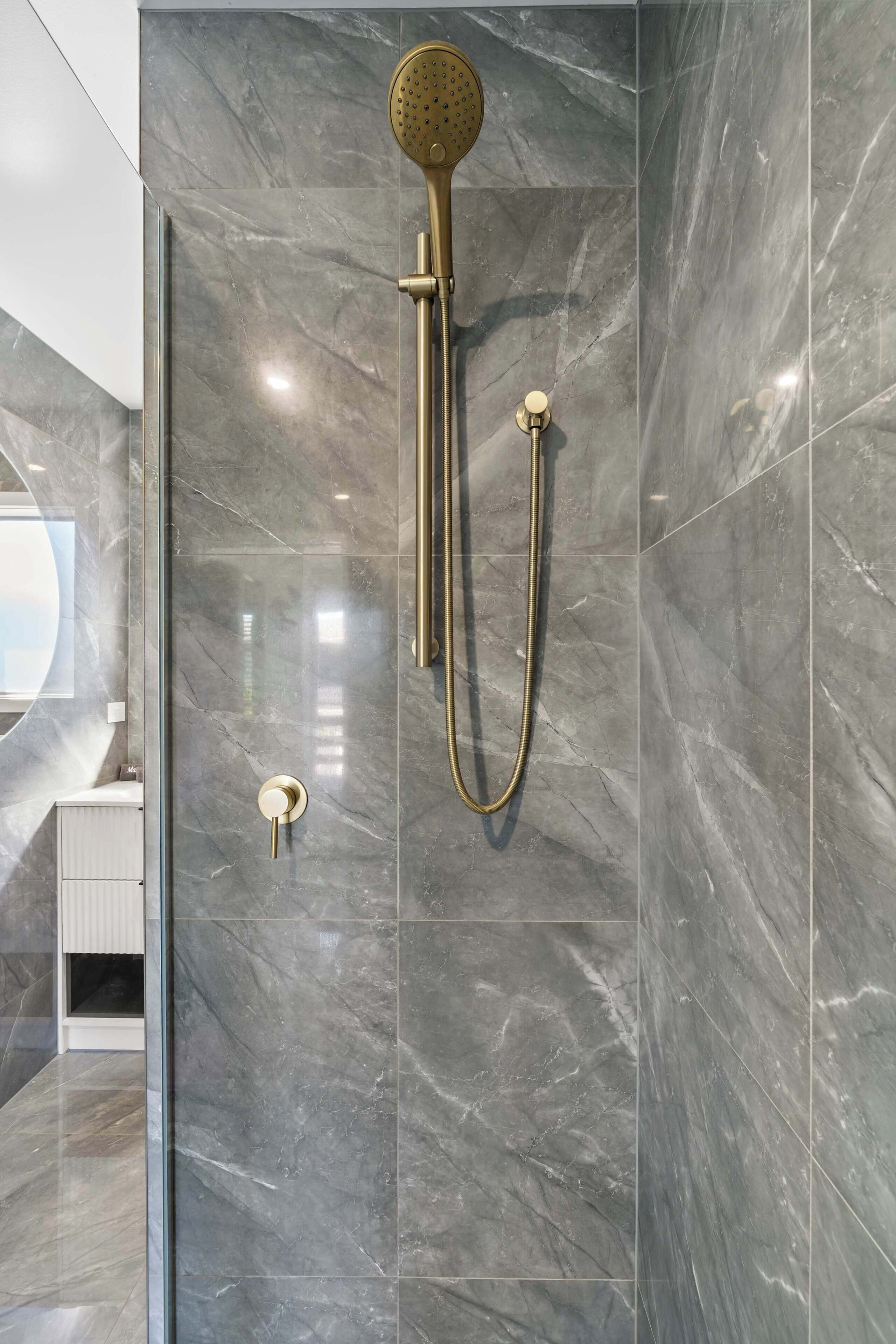 A modern bathroom with a shower, marble walls, and a glass door.