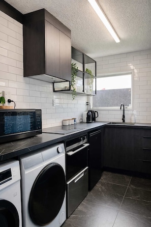 A modern kitchen with a washing machine, oven, and a window providing natural light. - Winifreds Apartment Where Design Meets Convenience (Hamilton)