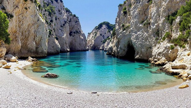Un paysage côtier avec une eau turquoise et limpide, des falaises rocheuses et une plage de galets.