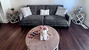 Un salon avec un canapé gris, une table basse ronde et un mur orné de cinq tableaux encadrés.