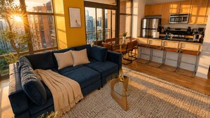 A modern living room with a sofa, a coffee table, and a view of the city through large windows.