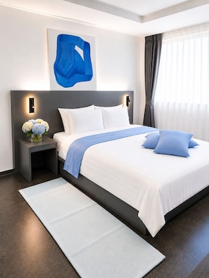 A modern hotel room with a large bed, a nightstand with a vase of flowers, and a blue abstract painting on the wall.
