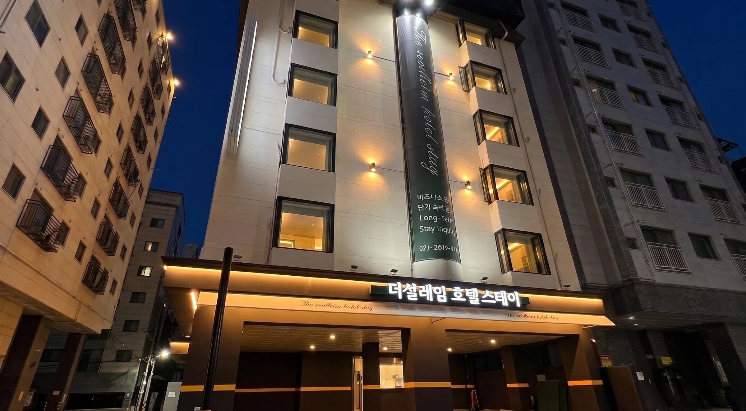 A hotel with a modern facade, illuminated windows, and a sign indicating it is a long-term stay hotel.