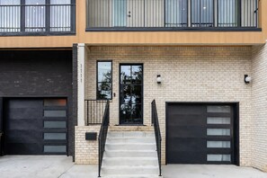 A modern two-story building with a brick facade, two garage doors, and a set of concrete steps leading to a small entrance. - 🌇 Skyline Views | Close to Broadway | Poker Table | Private Hot Tub | Sauna (Nashville)