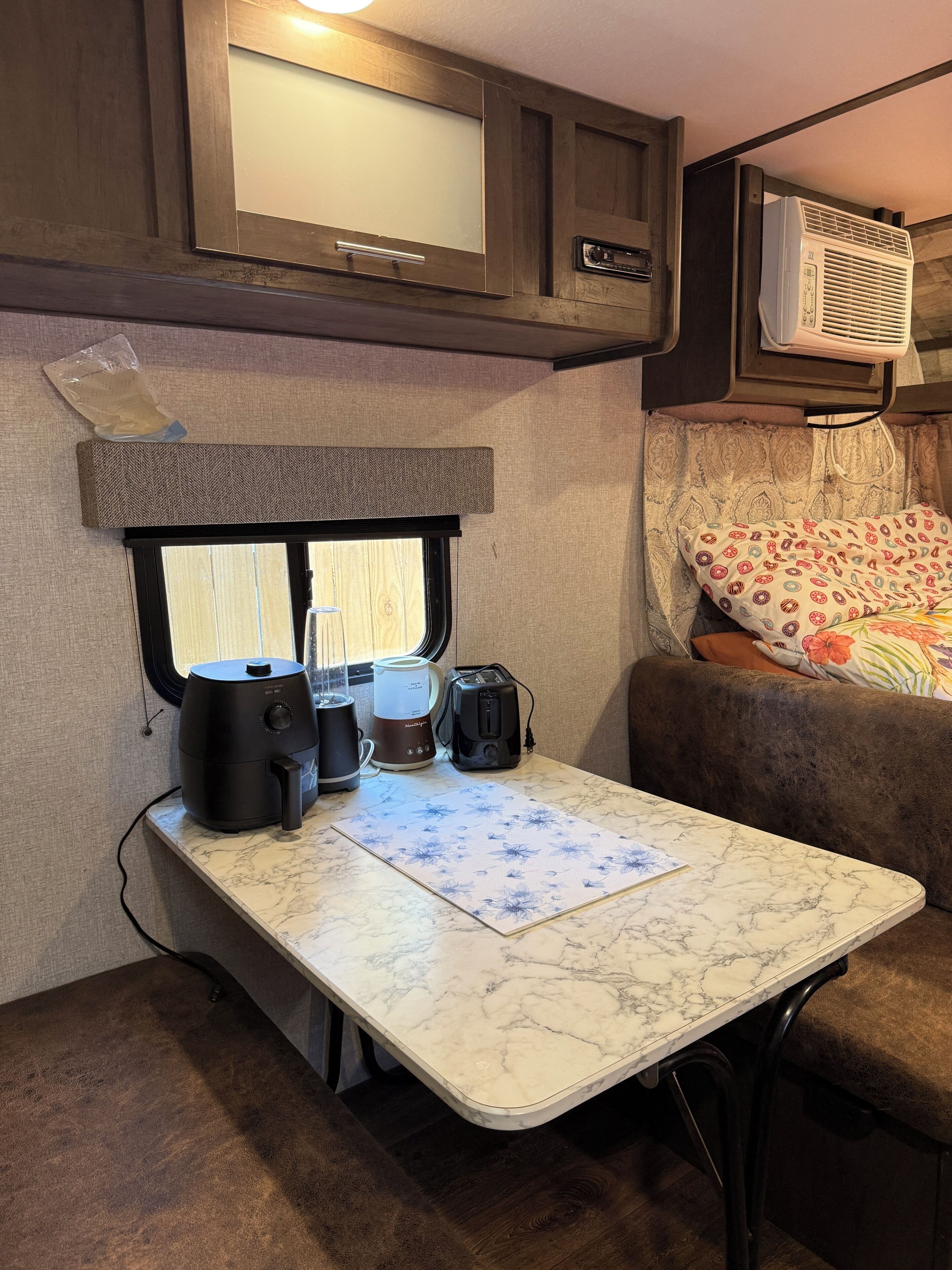 A compact RV interior with a kitchenette, a small table, a couch, and a window.