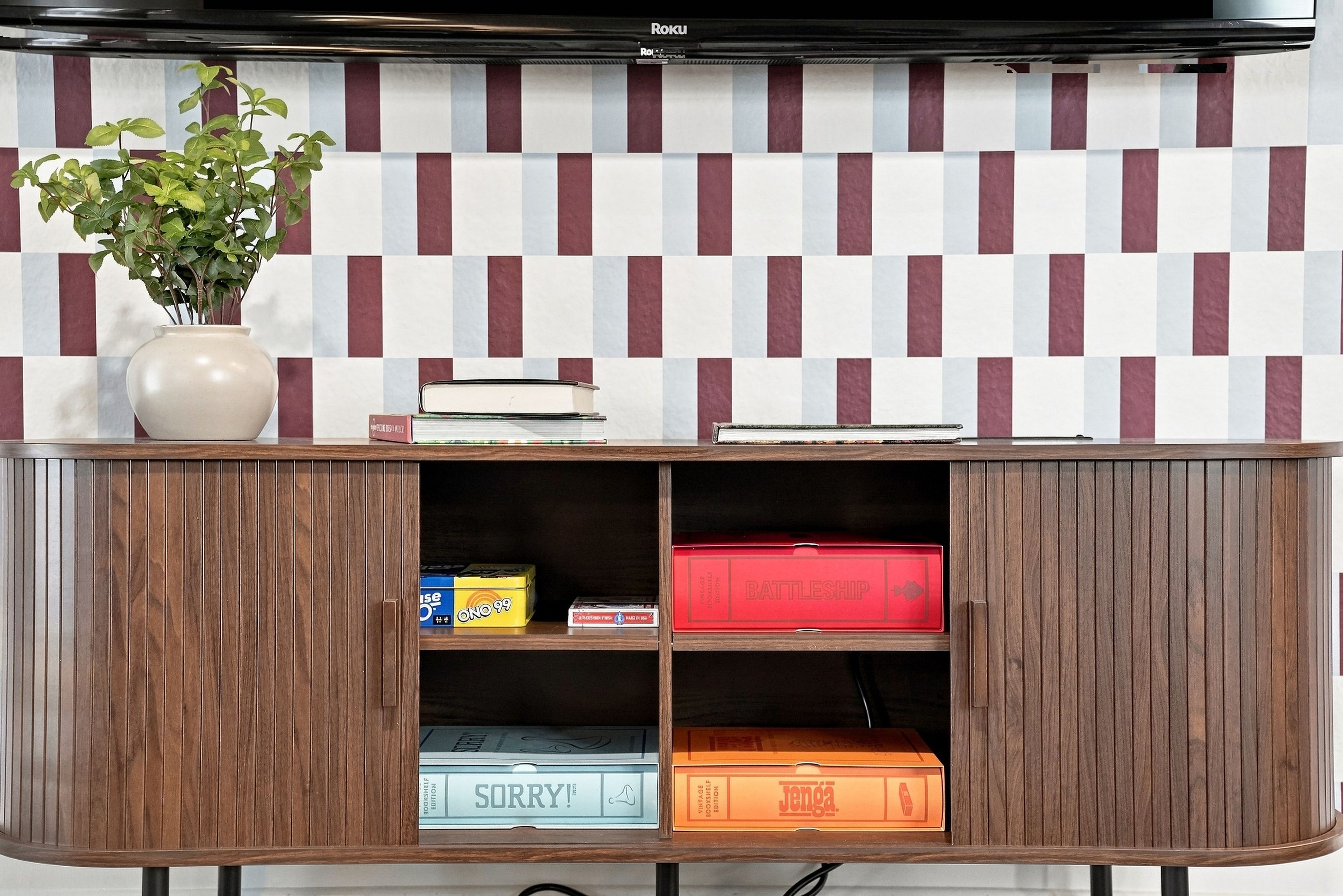 A wooden cabinet with a checkered wall pattern behind it, containing books, a plant, and storage boxes.