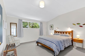 A bedroom with a bed, a chair, a nightstand, a window with curtains, and a ceiling light. - The Bach - Classic Kiwi Stay Opposite Pohara Beach (Pōhara)