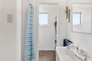 A bathroom with a shower curtain, a sink with a mirror, and a small window. - The Bach - Classic Kiwi Stay Opposite Pohara Beach (Pōhara)